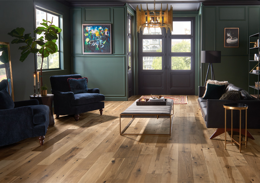 warm toned hardwood flooring in living room with leather couch and blue velvet accent chairs and maximalist decor